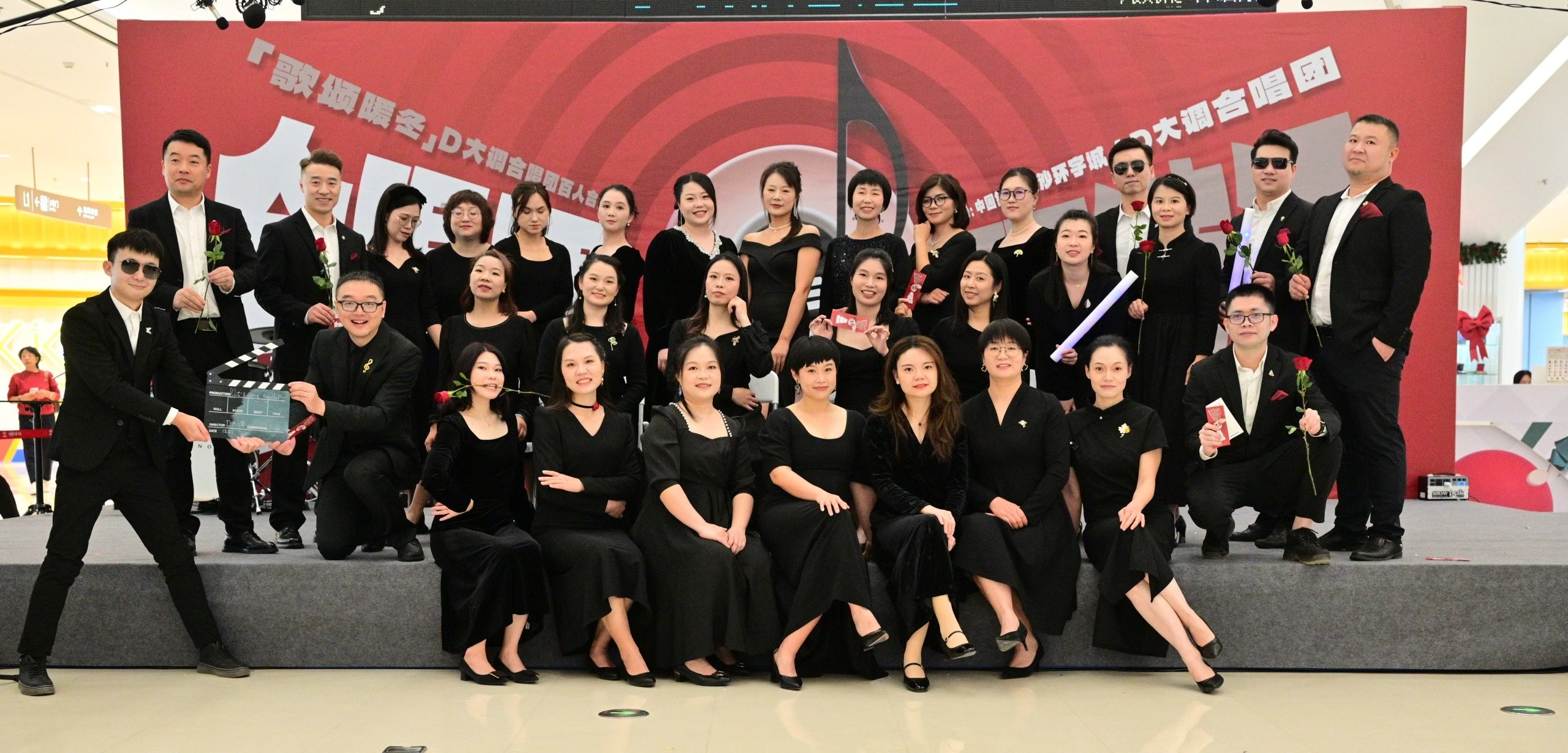Members of D Major Choir together in black concert dress before a red musical backdrop