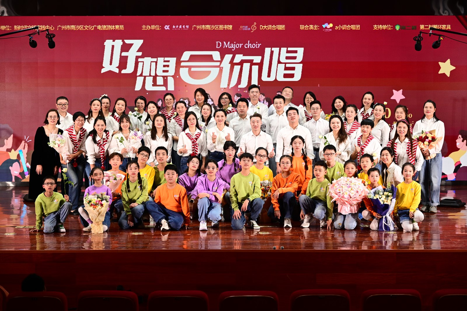 D Major Choir members and children posing before the red 好想合你唱 stage backdrop
