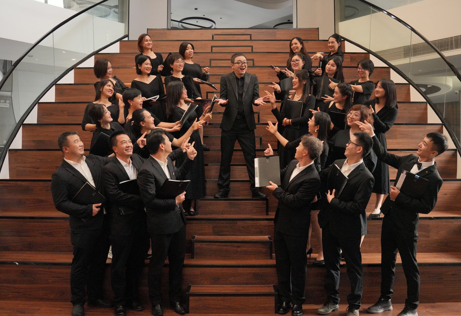 D Major Choir members in black concert dress sharing a laugh on wooden stairs